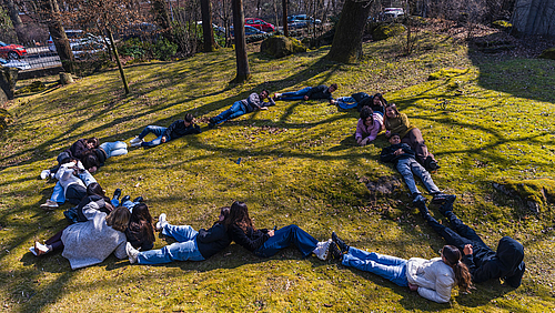 Jugendliche formen auf einer Wiese liegend ein Herz